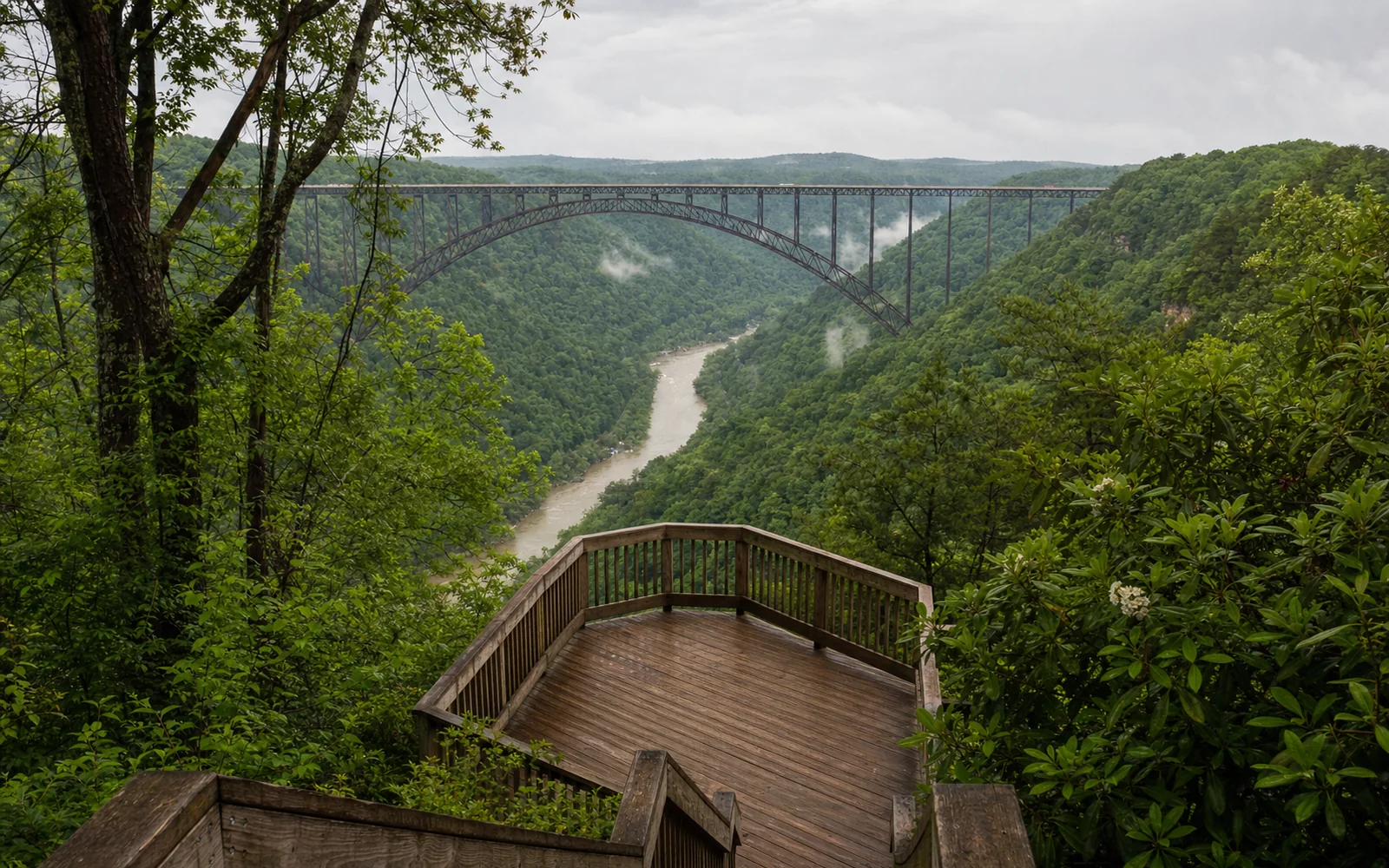 The Canyon Rim lower overlook platform in spring green, a timber deck with railings built out over the slope, the New River Gorge Bridge in full side view, AI-generated illustration