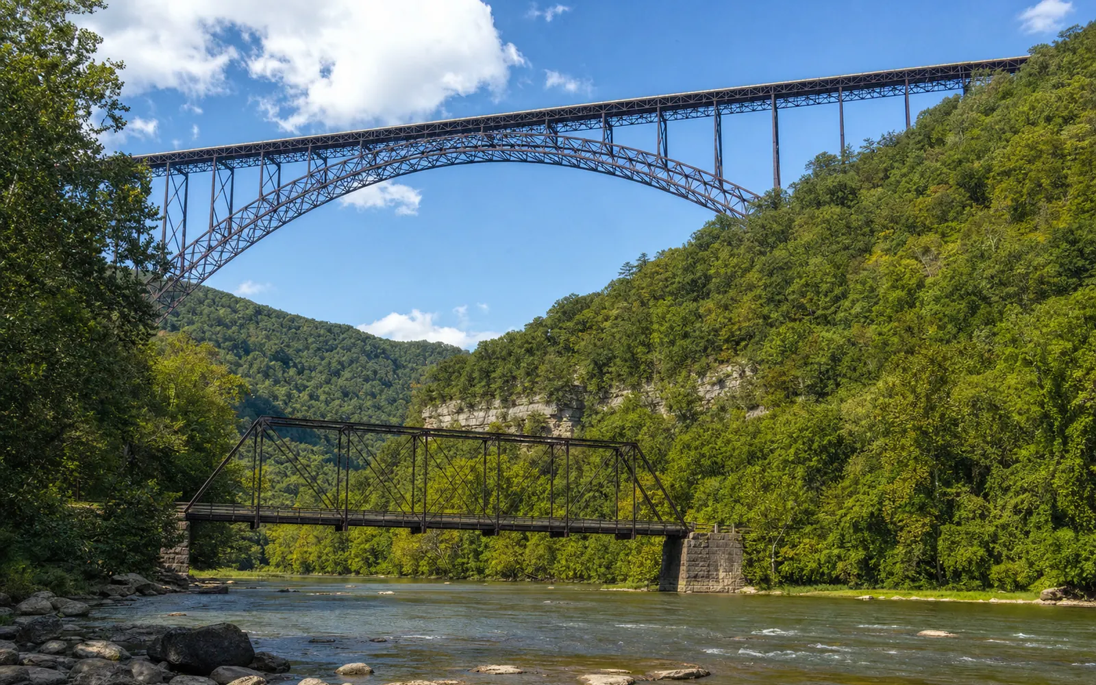 The one-lane Tunney Hunsaker steel truss bridge crossing the New River, with the arch of the New River Gorge Bridge high above it, AI-generated illustration