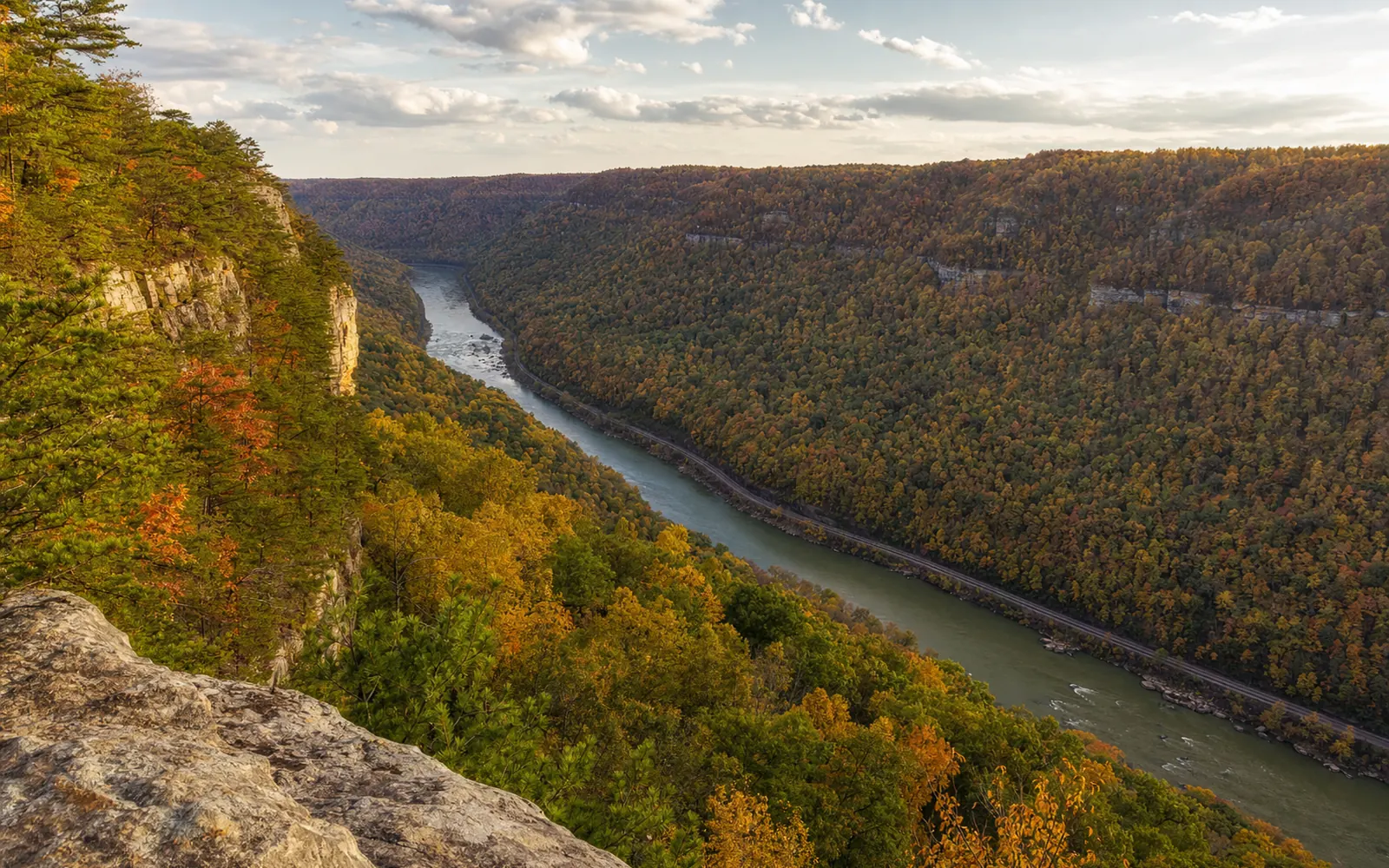The view from Grandview's North Overlook in October, the New River bending far below with railroad tracks along the water, peak color on the slopes, AI-generated illustration