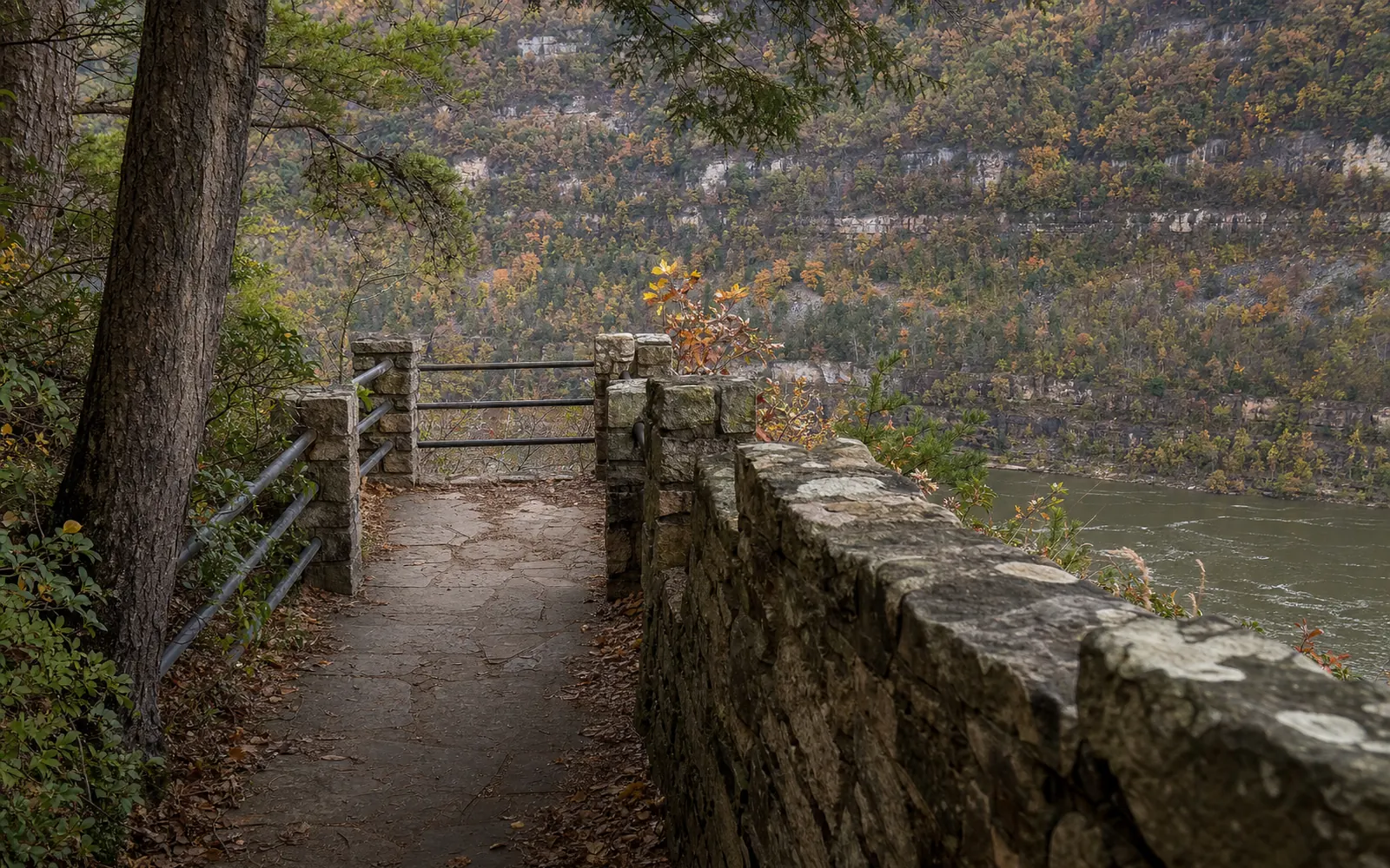 The short paved Overlook Trail at Hawks Nest, a walkway through the woods beside a rough sandstone CCC-era wall with railings leading toward the overlook, AI-generated illustration