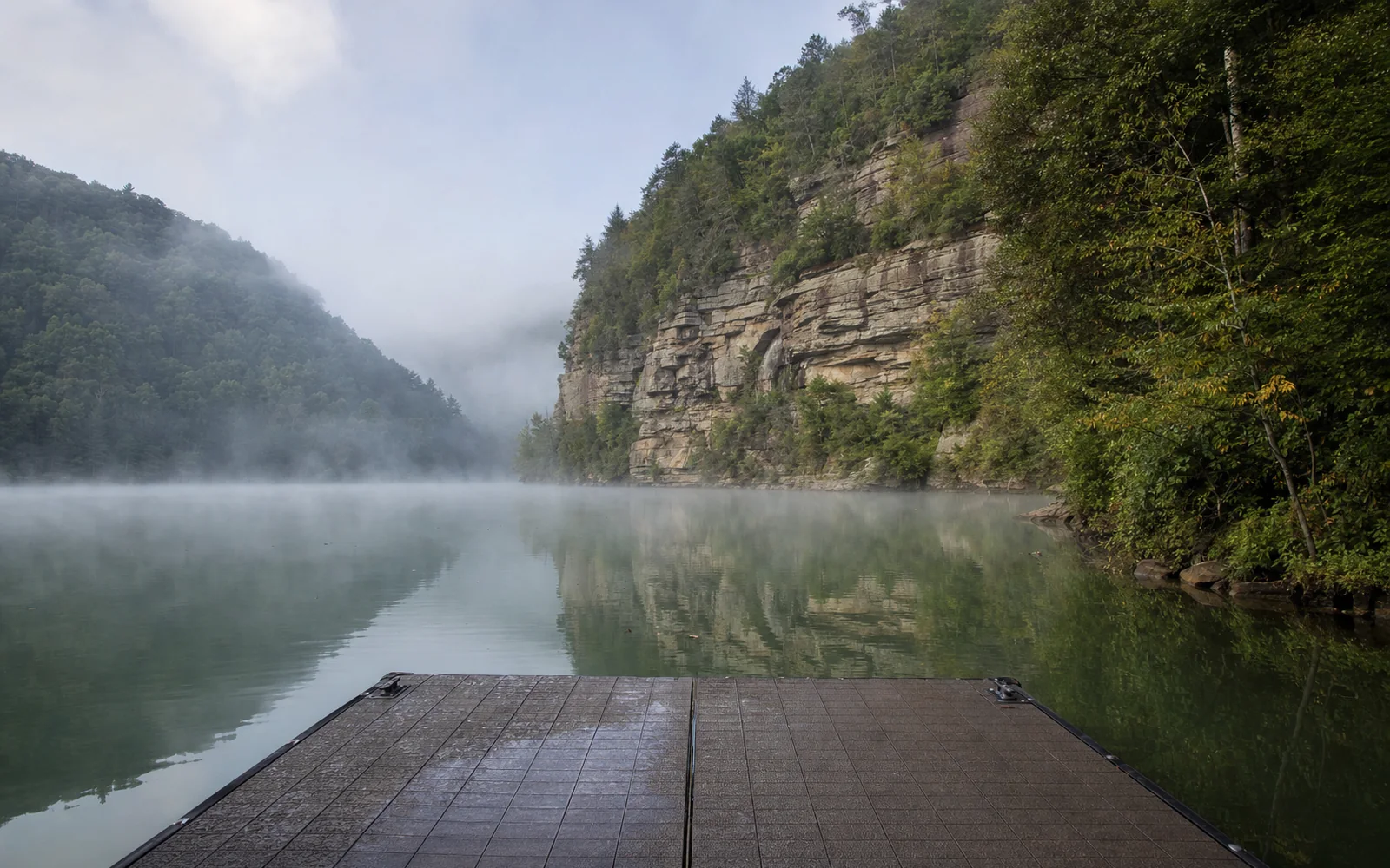 Hawks Nest Lake at river level, calm green water between steep forested gorge walls, a small floating dock, morning mist, AI-generated illustration