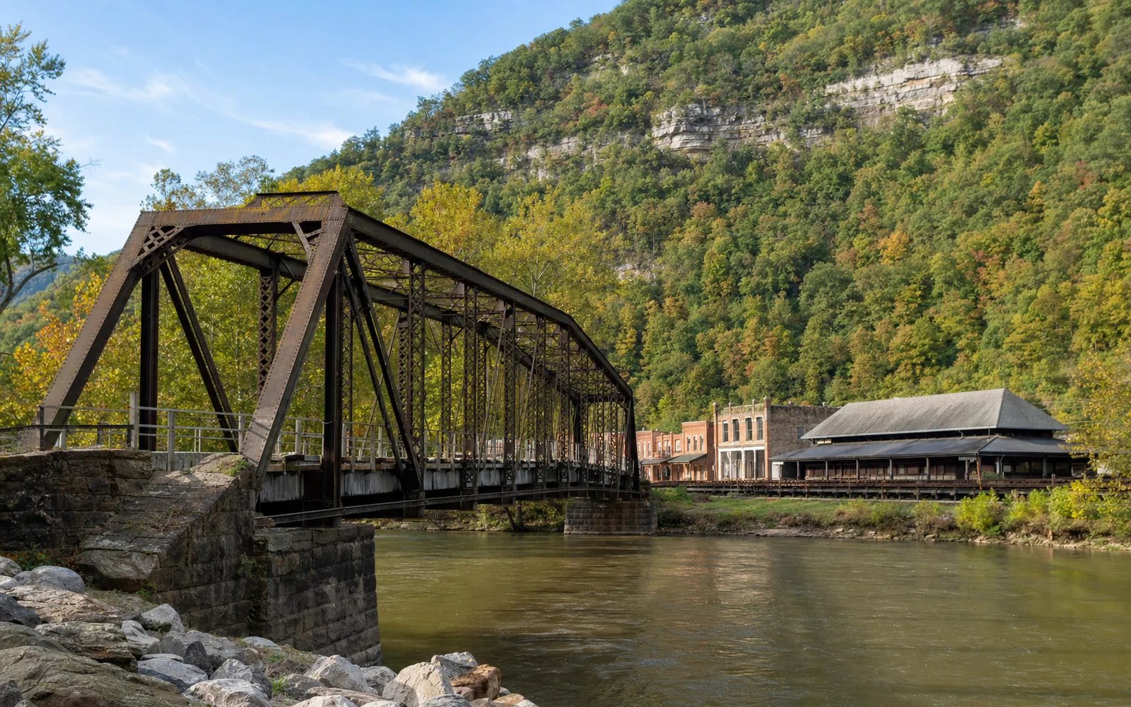 Thurmond's one-lane steel truss bridge crossing the New River toward the town, the small brick commercial row and the depot along the railroad tracks beyond, AI-generated illustration
