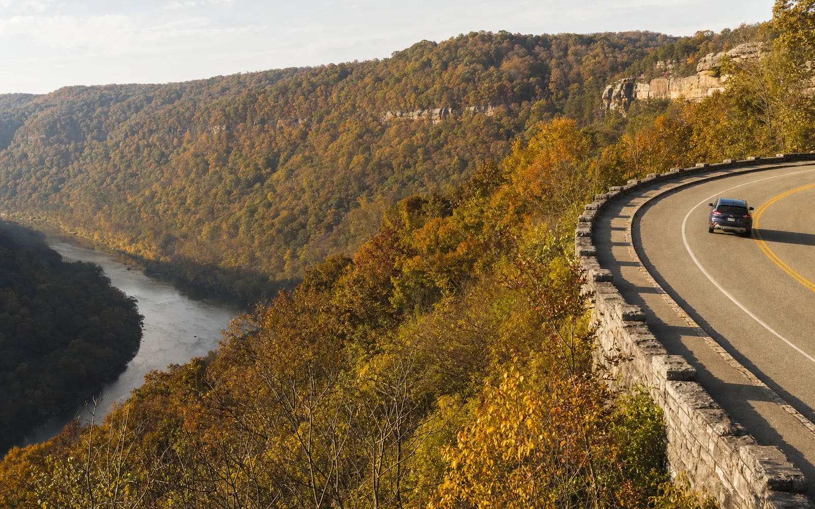 U.S. 60, the Midland Trail, curving along the gorge rim near Ansted with a low stone guardwall, fall color on the slopes, one car, AI-generated illustration