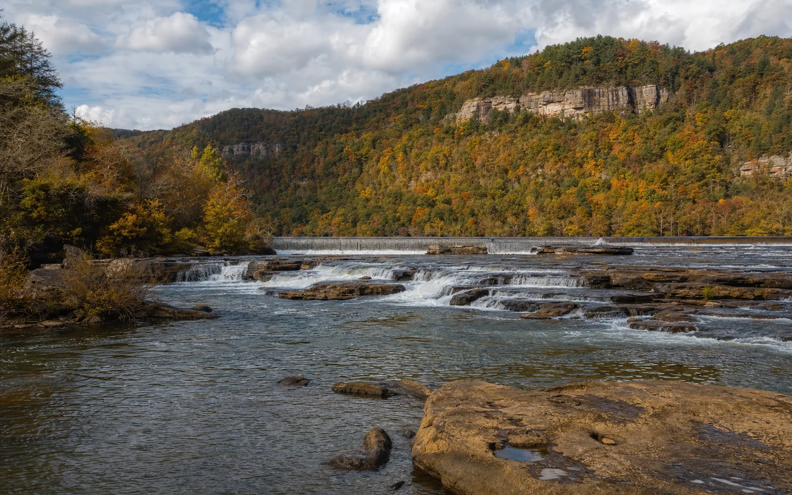 Kanawha Falls, a river-wide sandstone ledge on the broad Kanawha River with a low dam line behind, AI-generated illustration