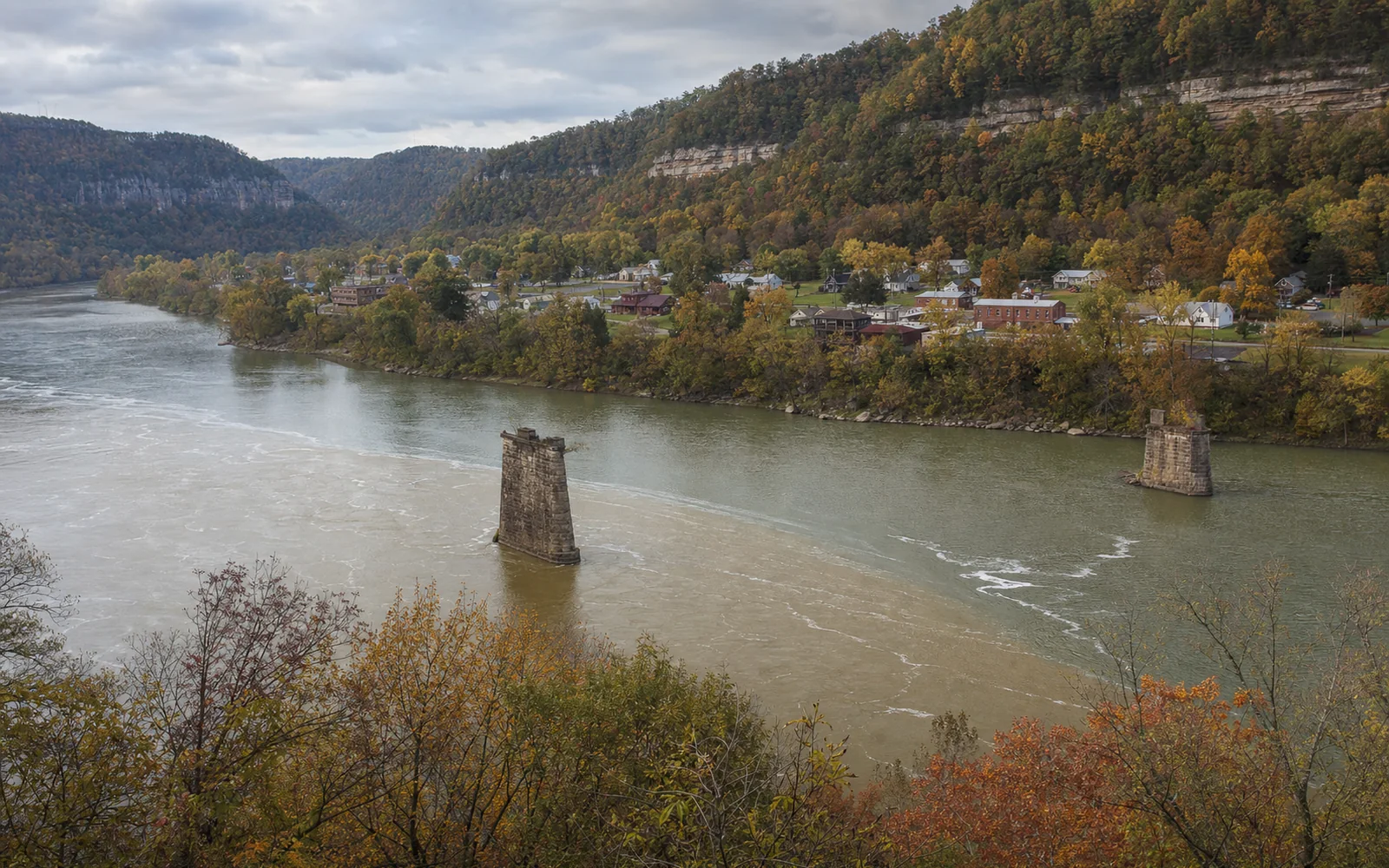The confluence at Gauley Bridge, the New and Gauley rivers meeting, old stone piers standing alone in the water, the small town on the bank, AI-generated illustration