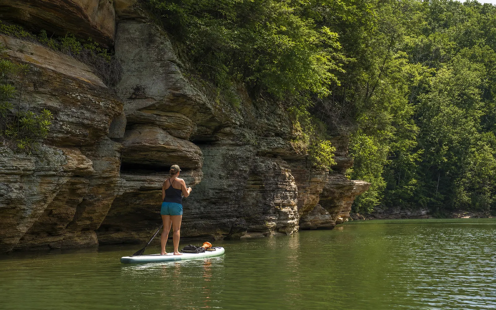 An adult paddleboarder gliding along Summersville Lake's sandstone cliffs over clear green water, AI-generated illustration