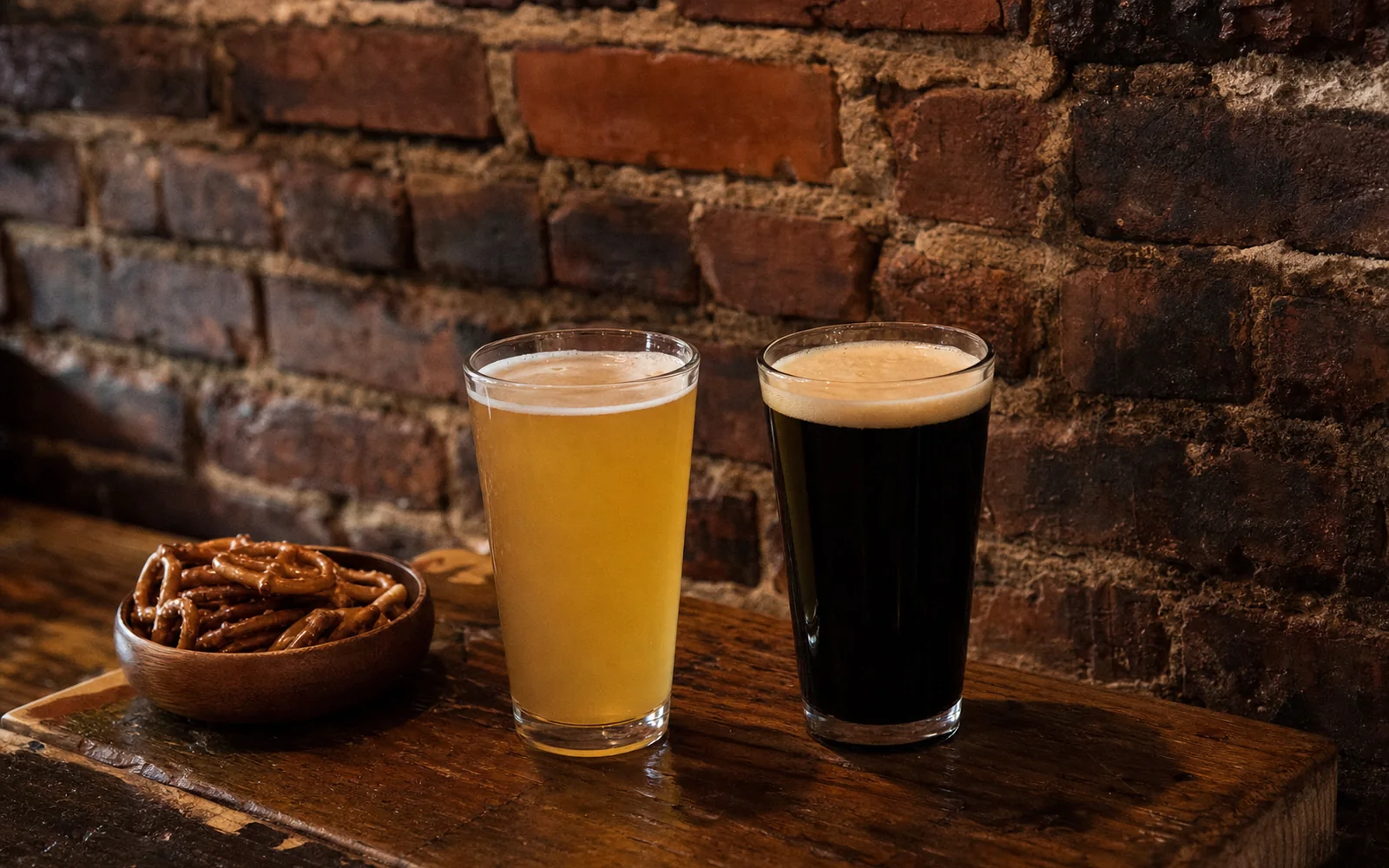 Two pints of craft beer, one pale and one dark, on a wooden bar top with a small bowl of pretzels and an exposed brick wall behind, AI-generated illustration