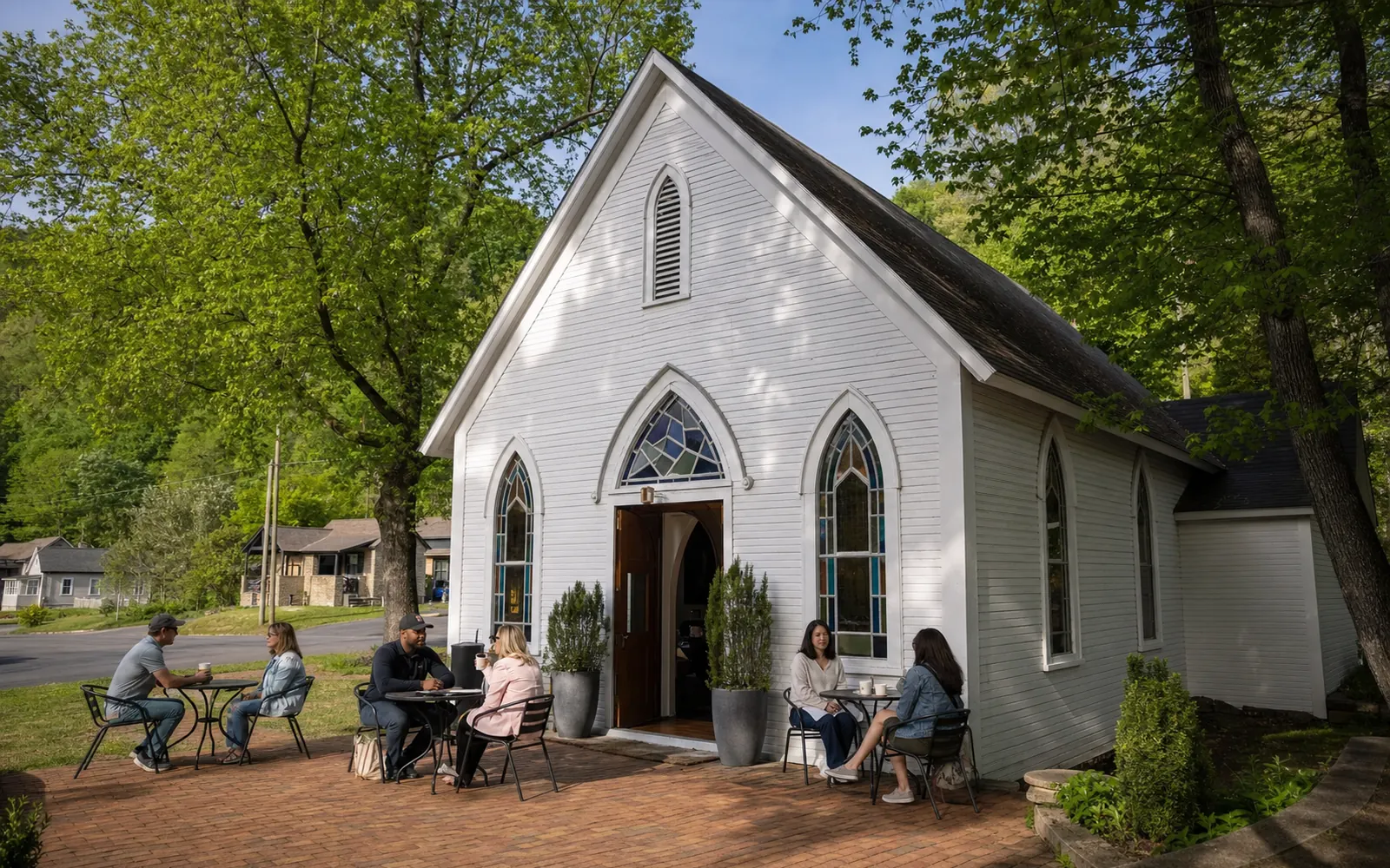 A white clapboard church with stained-glass windows on a small-town street, with adults seated at bistro tables out front, AI-generated illustration