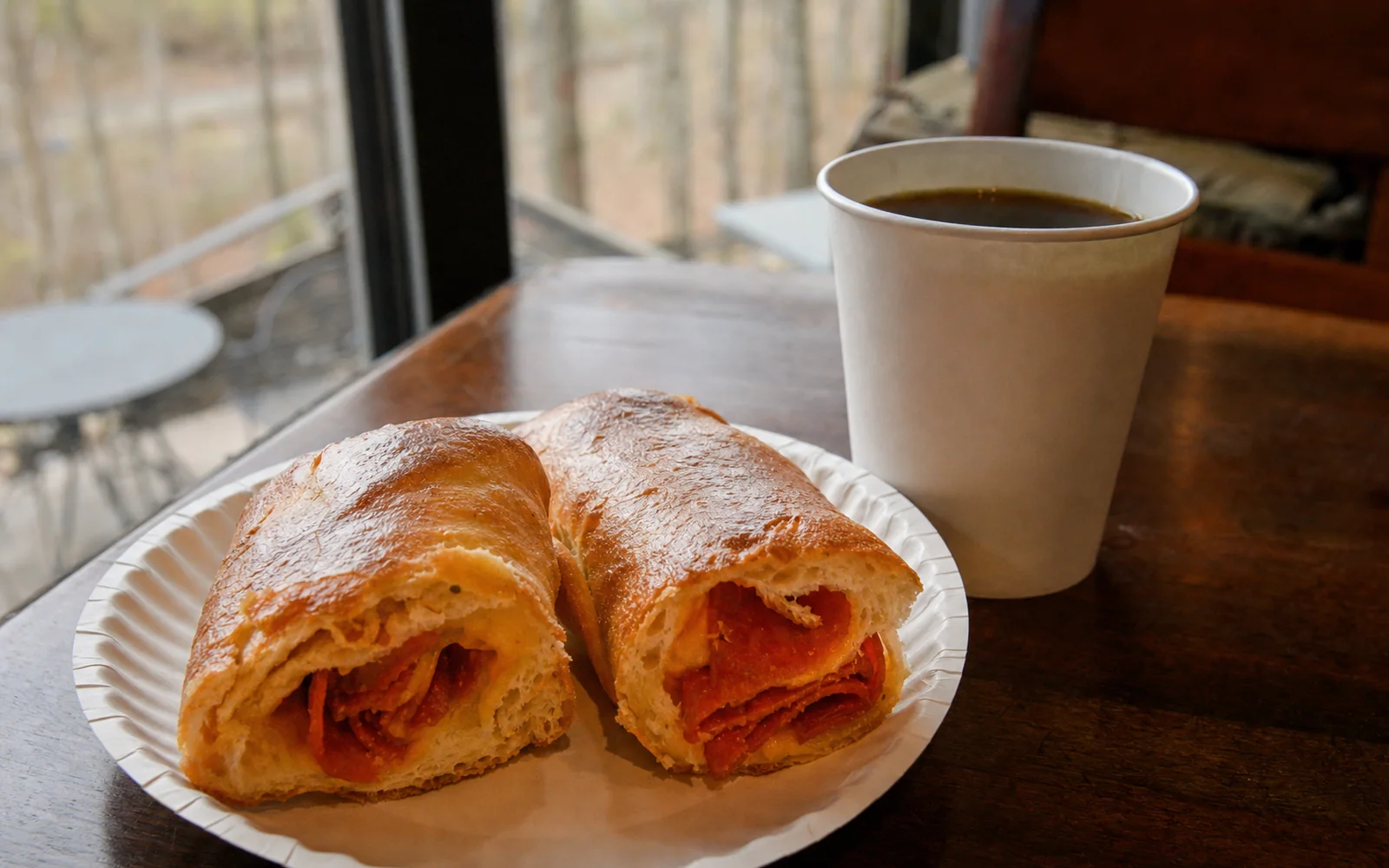 A West Virginia pepperoni roll split open on a paper plate beside a paper cup of coffee on a wooden table, AI-generated illustration