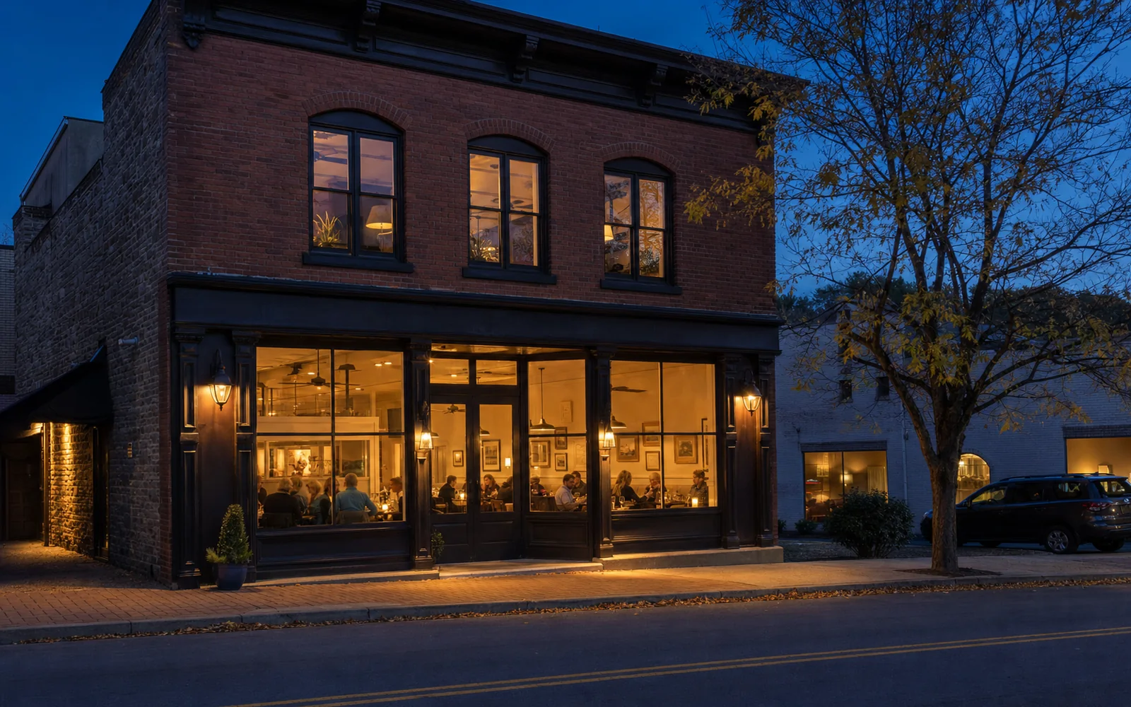 A two-story brick storefront on a small-town street at evening with big lit windows and blurred diners inside, AI-generated illustration
