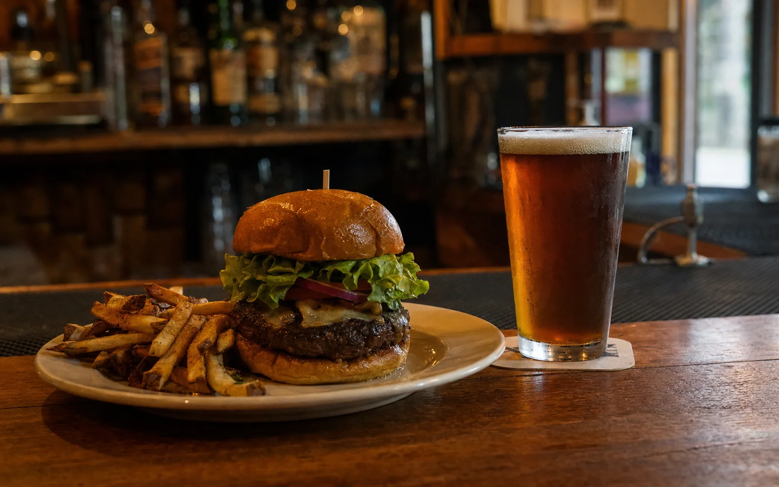 A burger with fries and a pint of amber beer on a bar top, AI-generated illustration