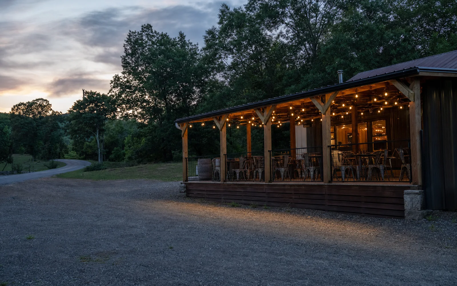 A roadside tap house with a covered porch and string lights at dusk, a gravel lot, wooded hills, AI-generated illustration