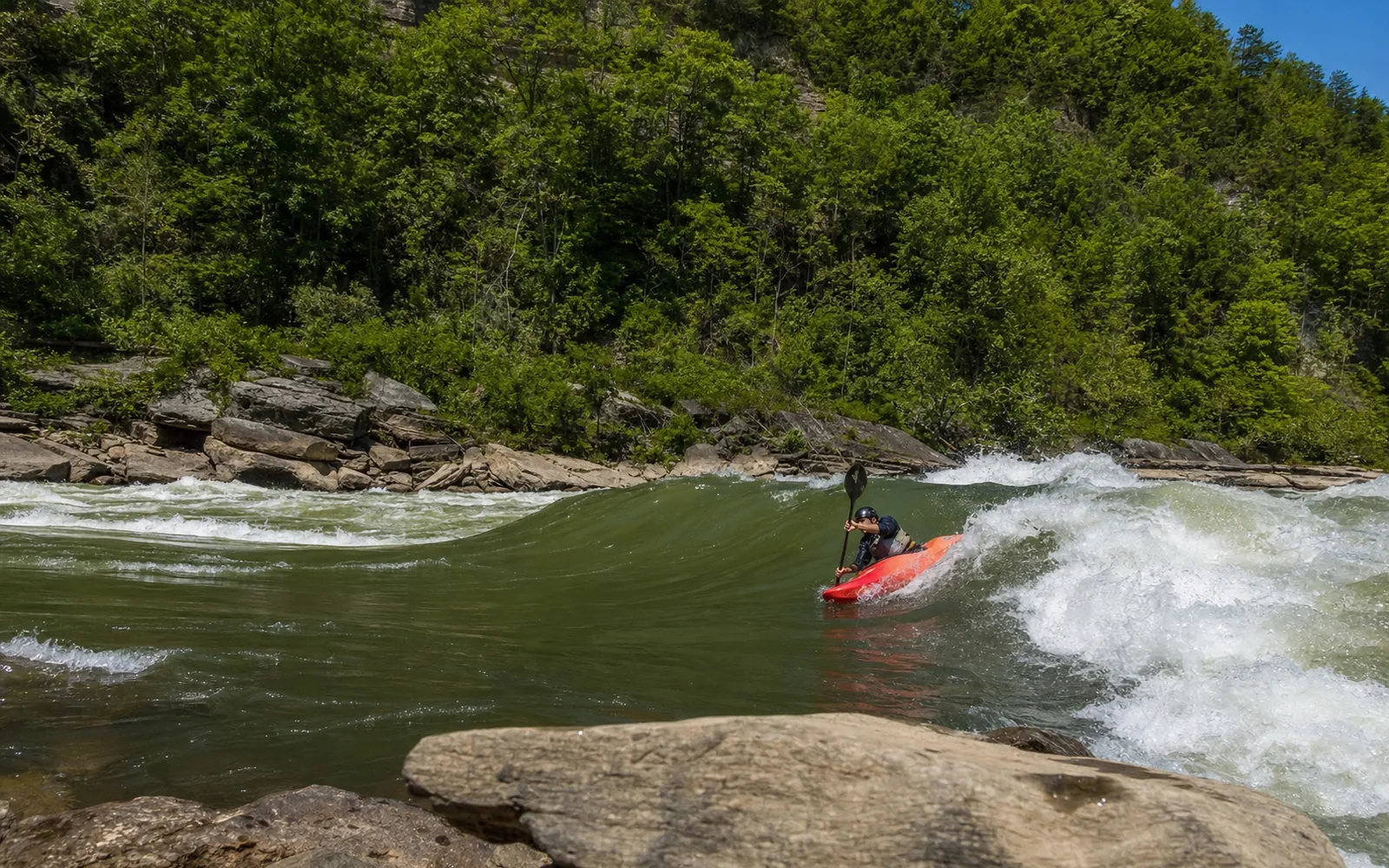 An adult paddler in a whitewater kayak surfing a green wave on the New River, gorge walls behind, AI-generated illustration