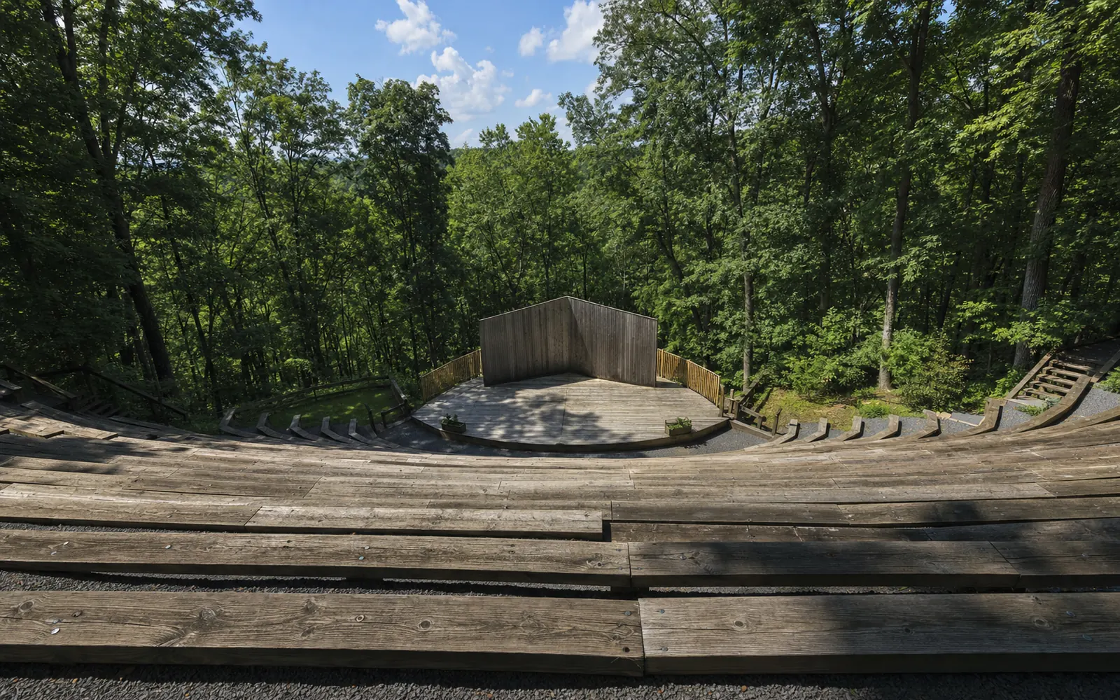 Empty tiered wooden benches of an outdoor amphitheatre descending to a stage in the forest, afternoon, AI-generated illustration