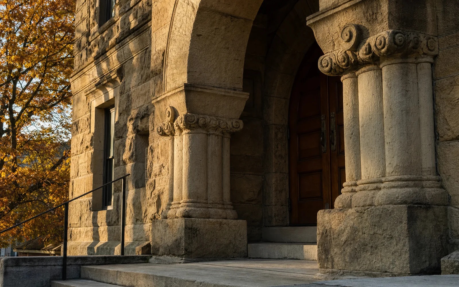 Close detail of the Fayette County Courthouse's arched sandstone entrance with rough-faced stone blocks, carved column capitals and heavy wooden doors, AI-generated illustration