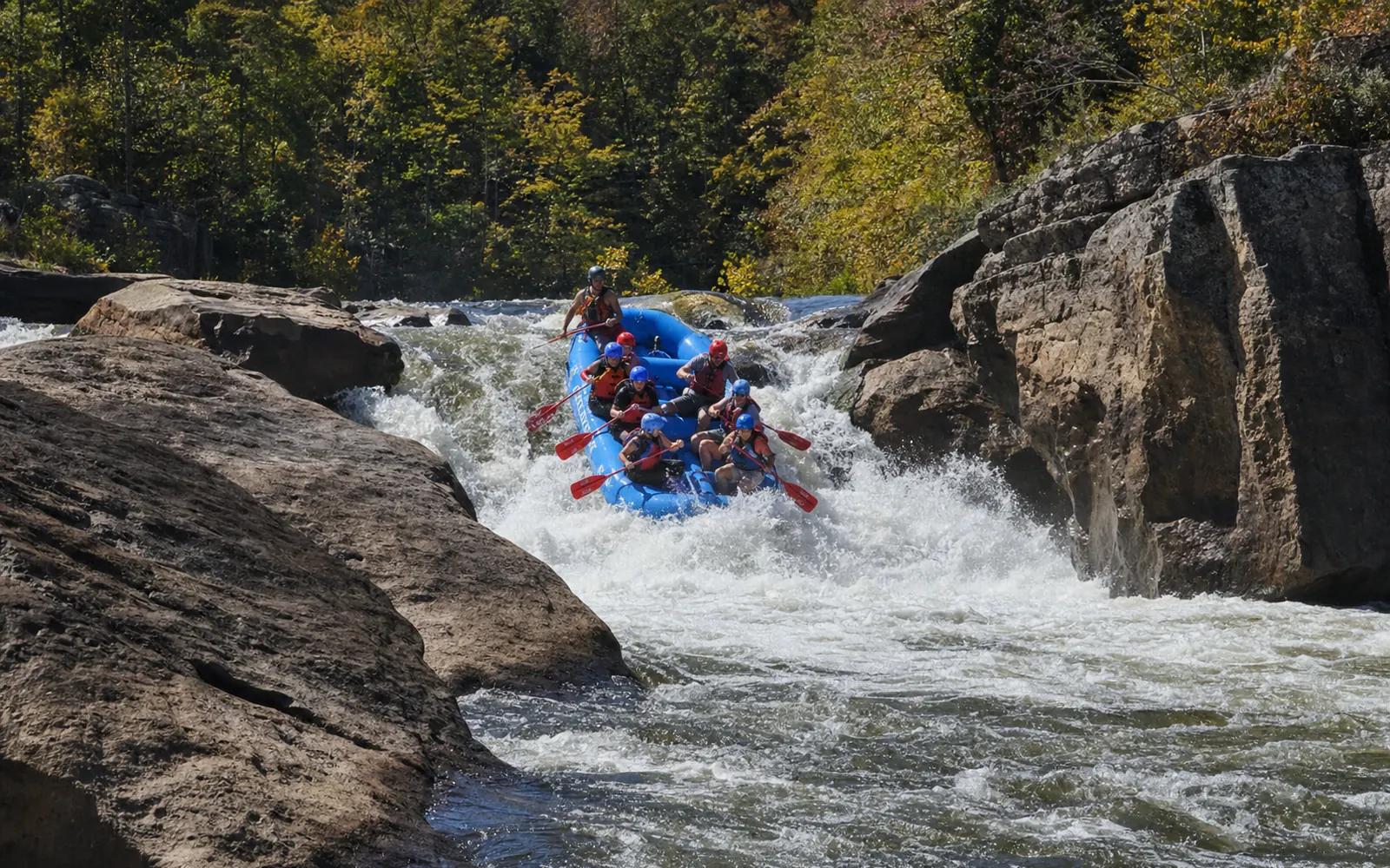 A raft of adult paddlers and a guide dropping over a clean ledge drop on the Upper Gauley, big boulders at both sides, whitewater exploding, AI-generated illustration