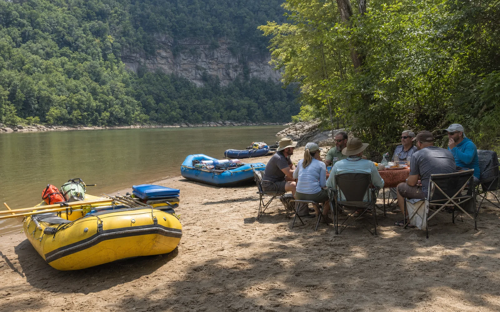 Rafts pulled up on a sandy river beach for lunch in the Lower New gorge, adult guests and guides at a folding table, forested walls rising behind, AI-generated illustration
