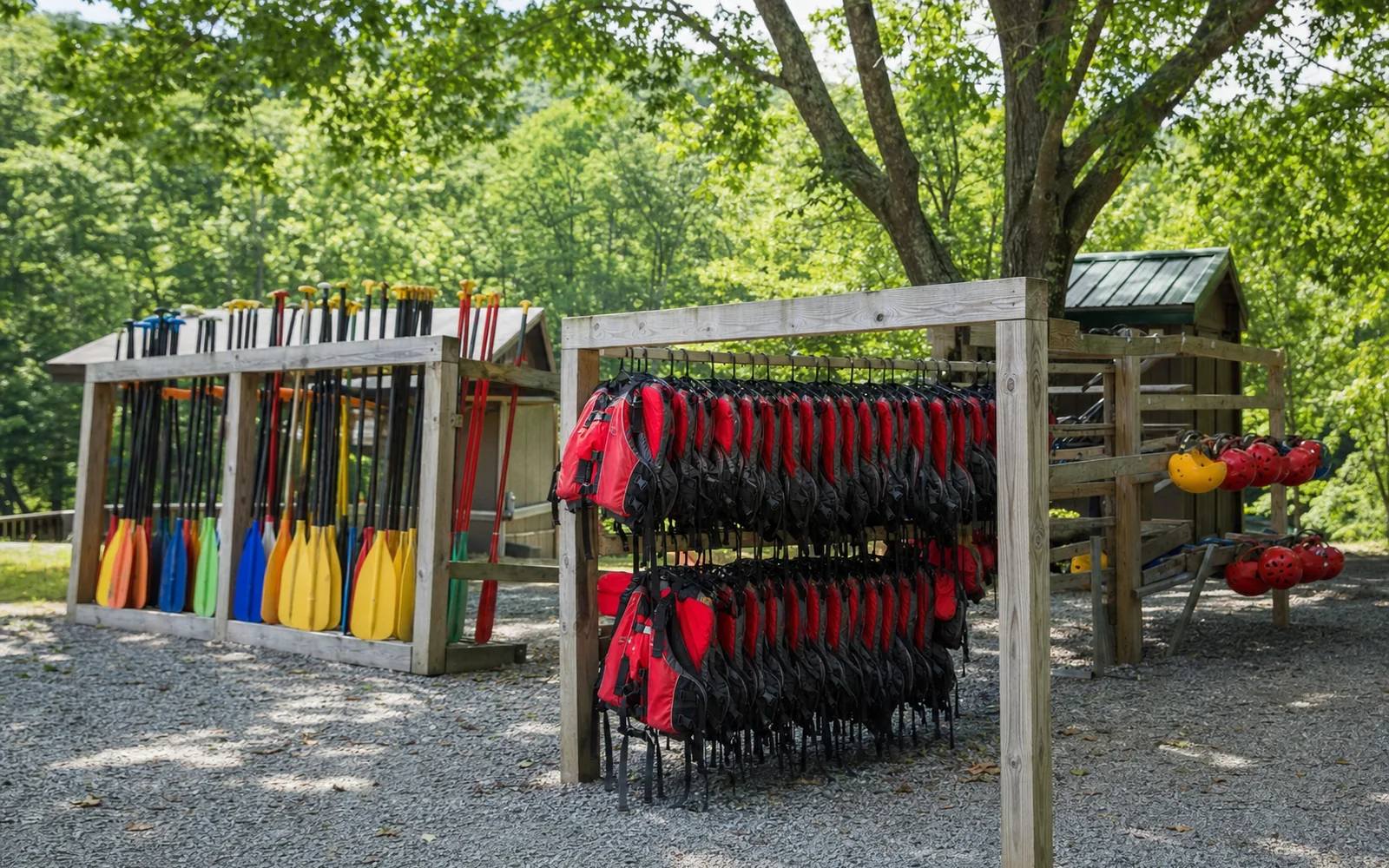 Racks of paddles, helmets and life jackets drying in the sun at an outfitter's base, gravel yard, oak trees, AI-generated illustration