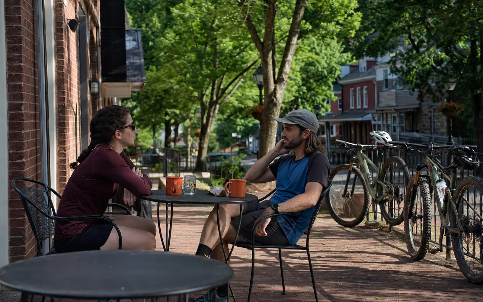 Two adults at an outdoor cafe table on a brick sidewalk on Court Street in the morning, mountain bikes leaning on a rail, brick storefronts, AI-generated illustration