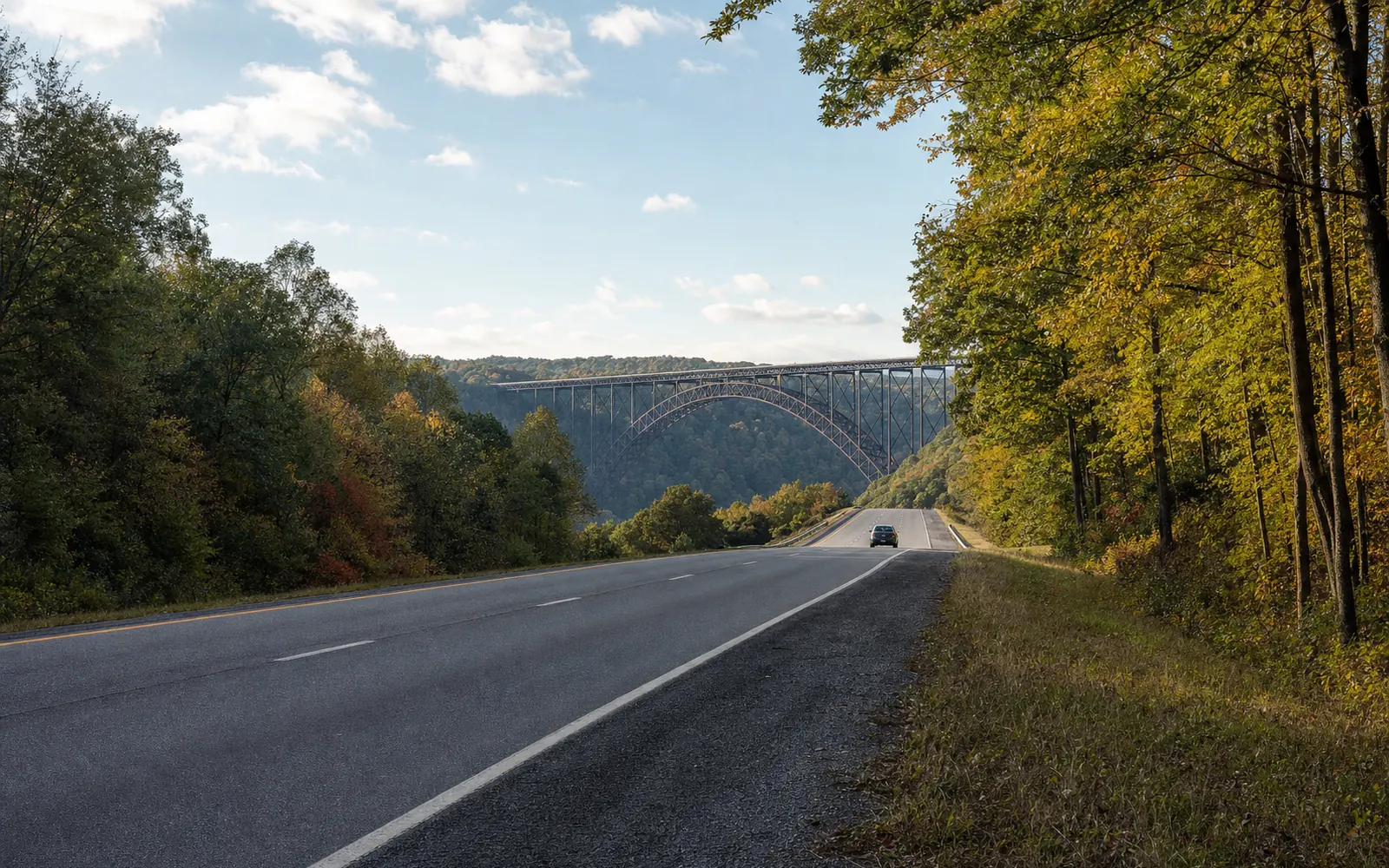 A four-lane highway running between autumn woods toward a steel arch bridge spanning a forested gorge, with one car on the road under a blue sky, AI-generated illustration