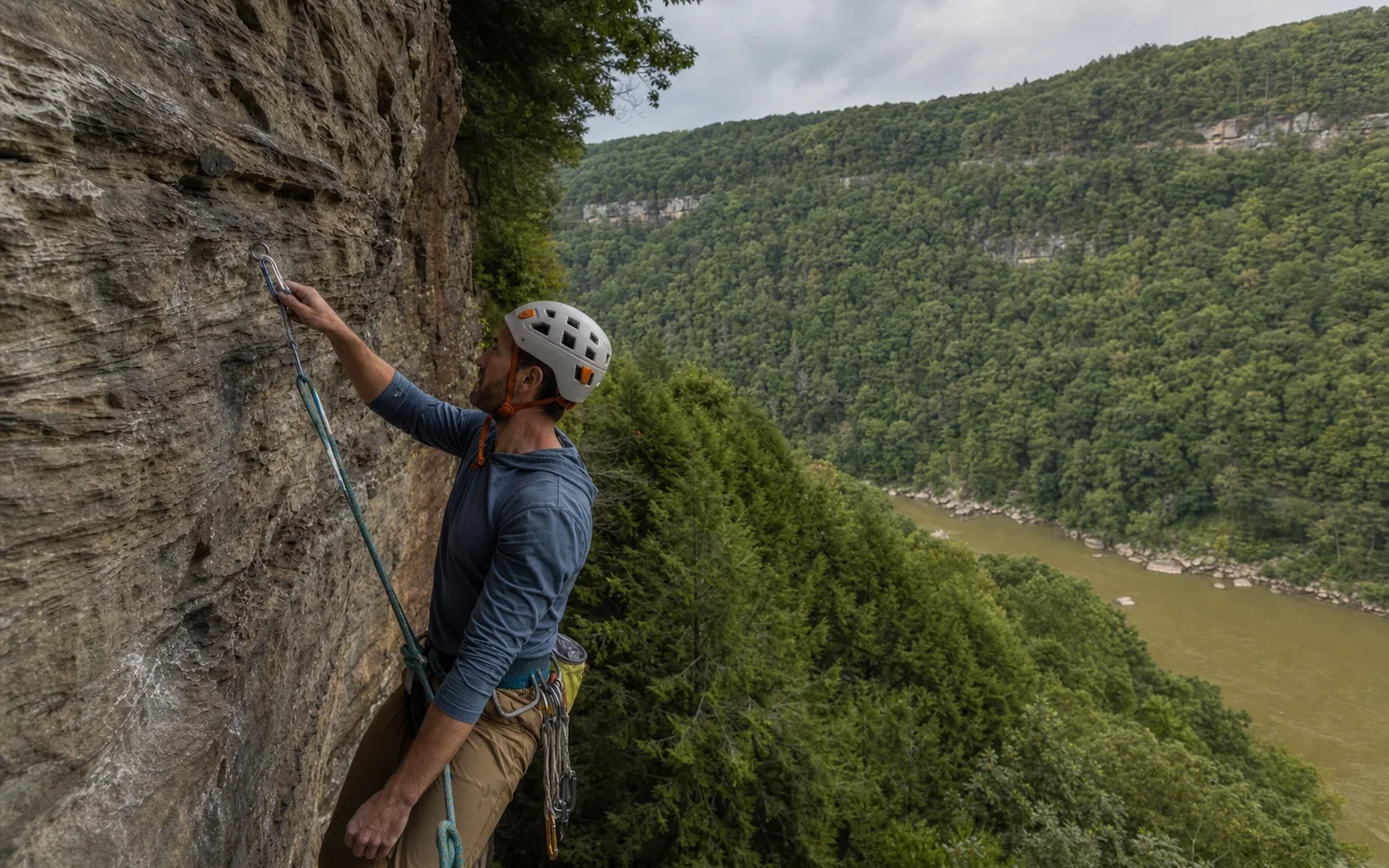 An adult climber in a helmet clipping a quickdraw on a Nuttall sandstone wall, seen from the side, hemlocks below, AI-generated illustration