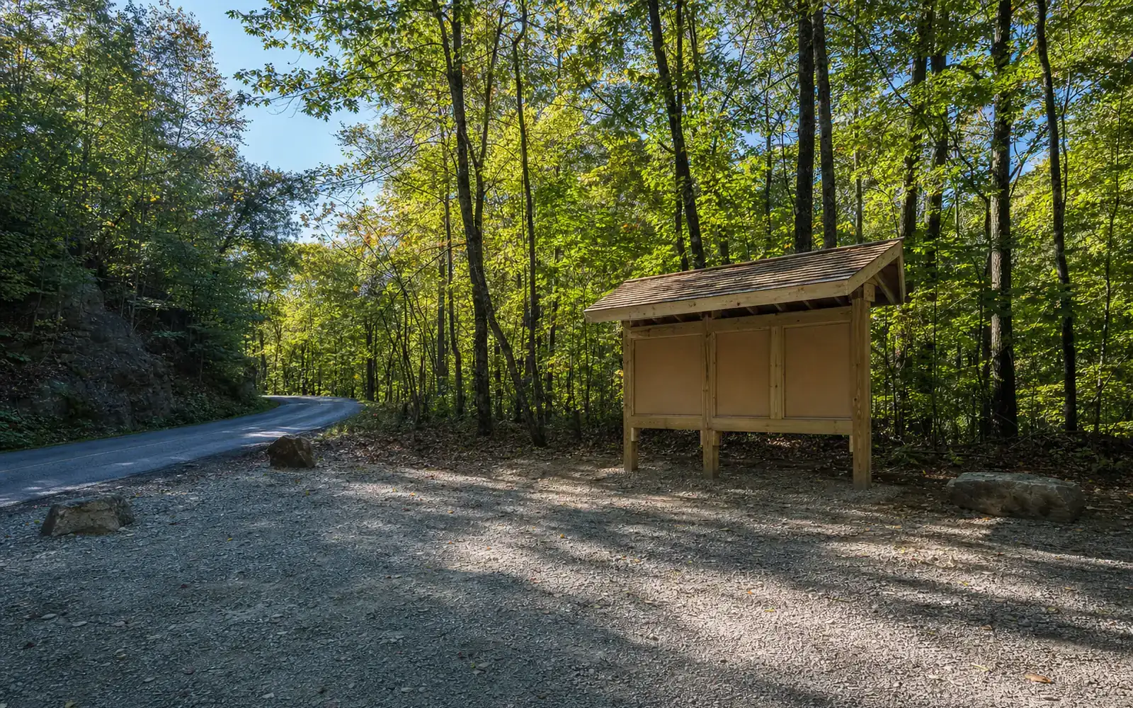 A freshly graveled trailhead parking area with a new timber kiosk with blank panels at the edge of hardwood forest, AI-generated illustration