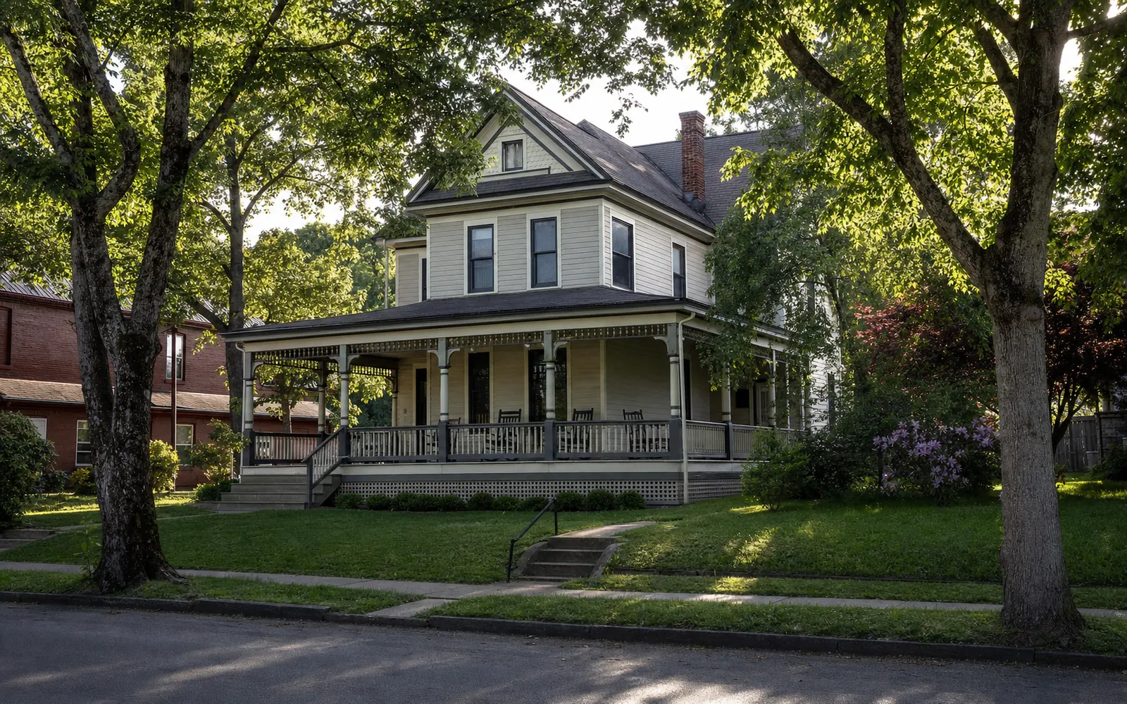 A two-story Victorian frame house with a wraparound porch and rocking chairs on a tree-lined small-town street, bed-and-breakfast feel, AI-generated illustration