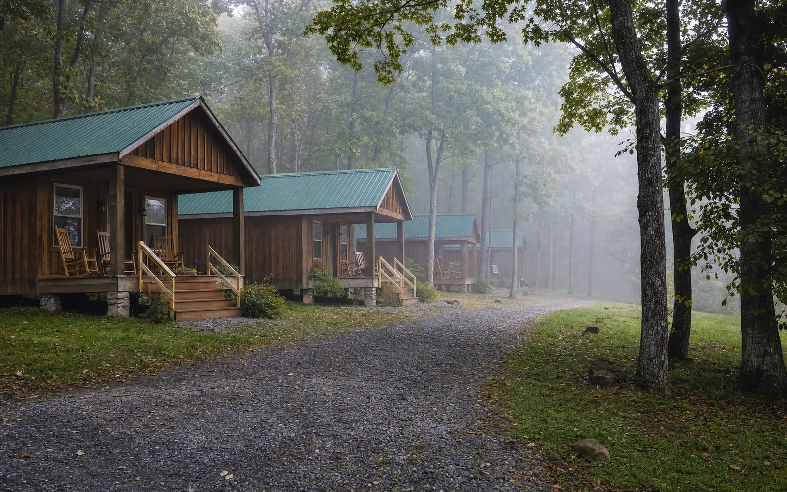 A row of small rental cabins along a gravel lane on a wooded ridge, morning mist between the trees, porches with chairs, AI-generated illustration