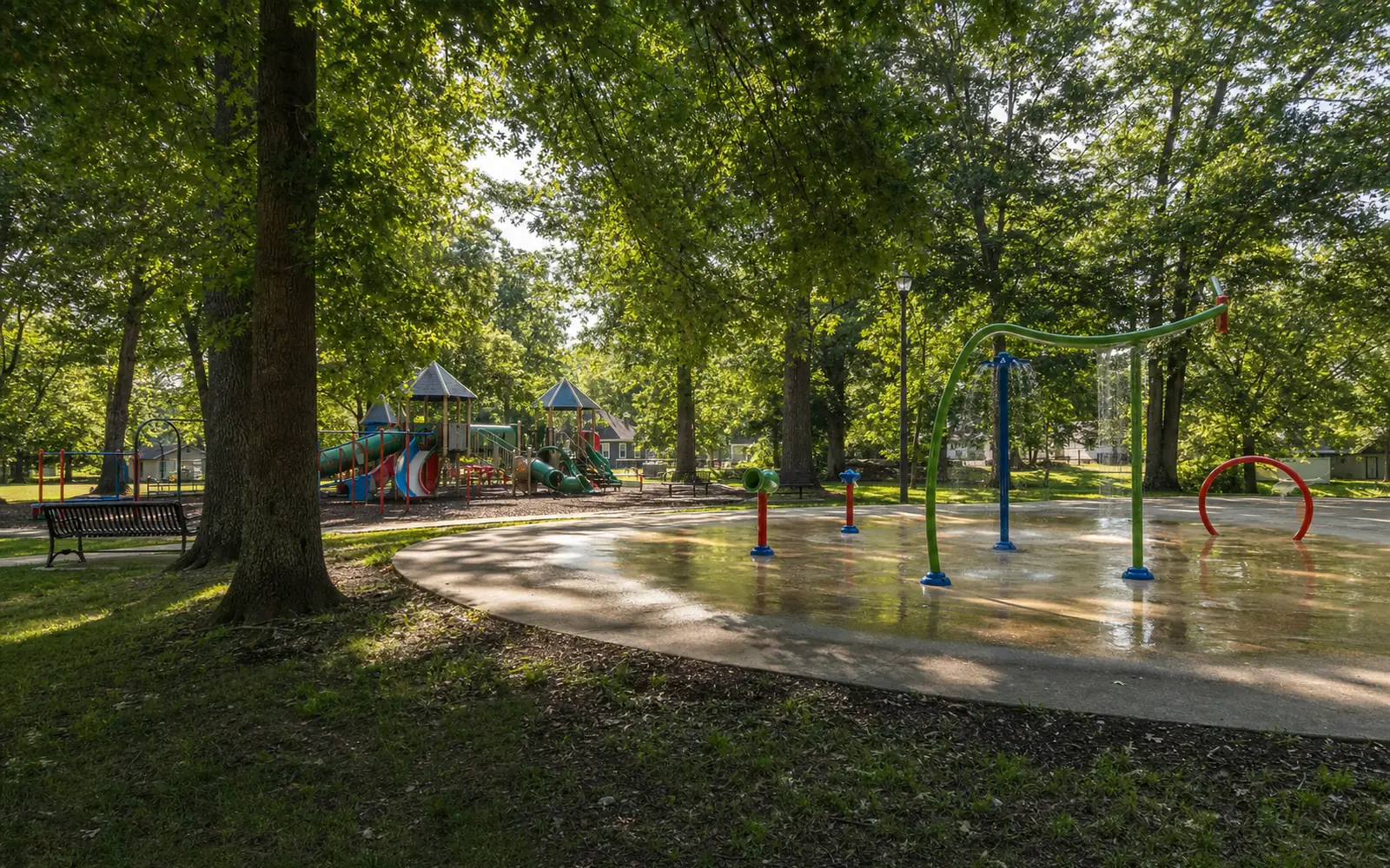 A town park splash pad and colorful playground among oak trees in the morning, AI-generated illustration