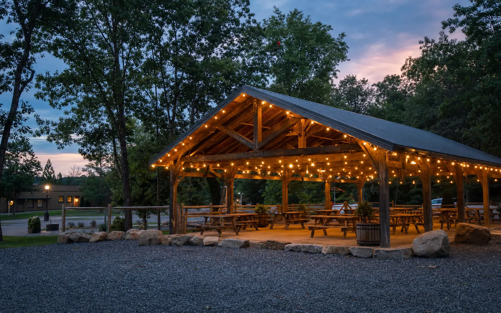 A timber-frame pavilion at an adventure resort at dusk with string lights and picnic tables, AI-generated illustration