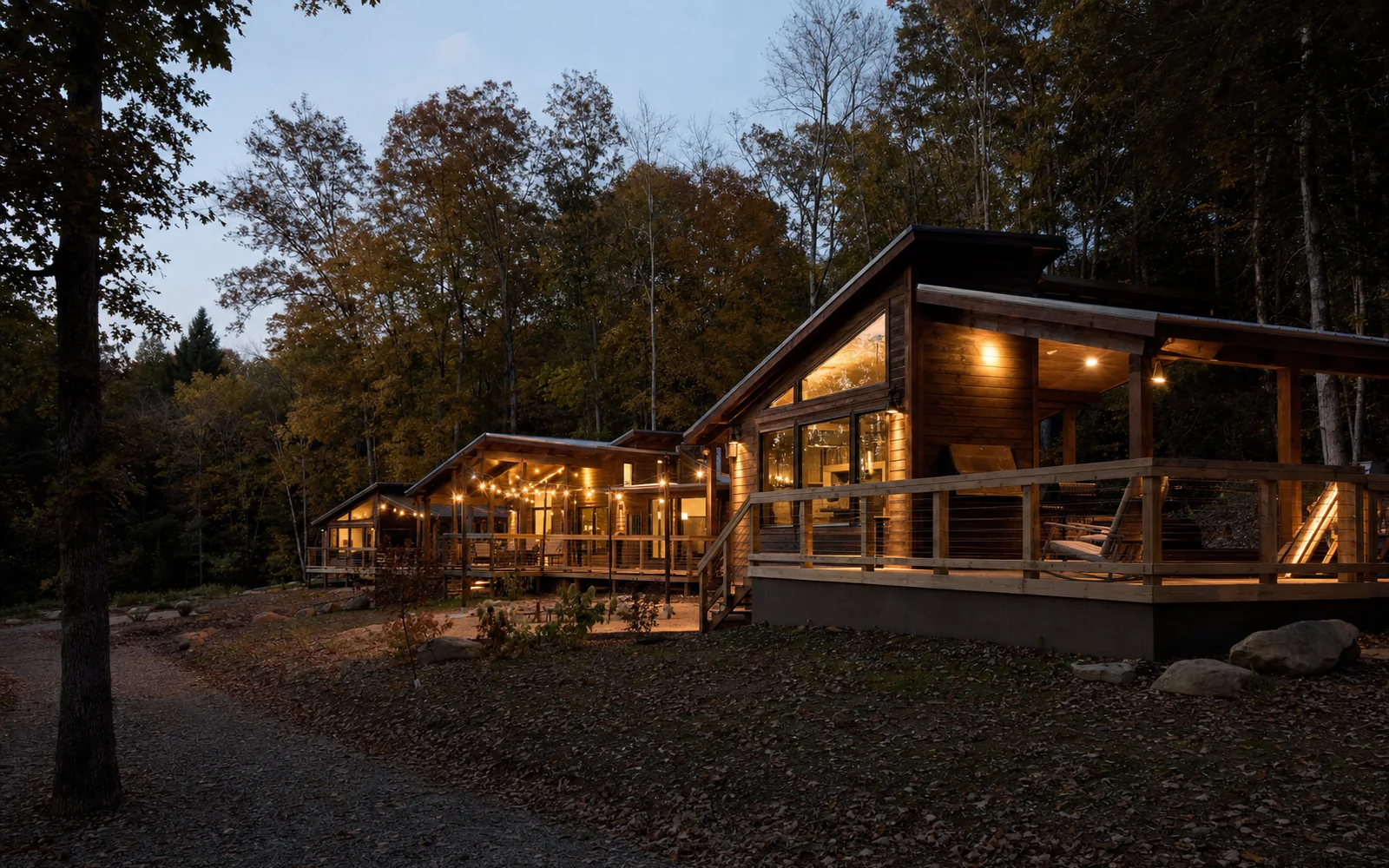 A cluster of modern timber cabins with decks among trees at dusk, lights on, AI-generated illustration