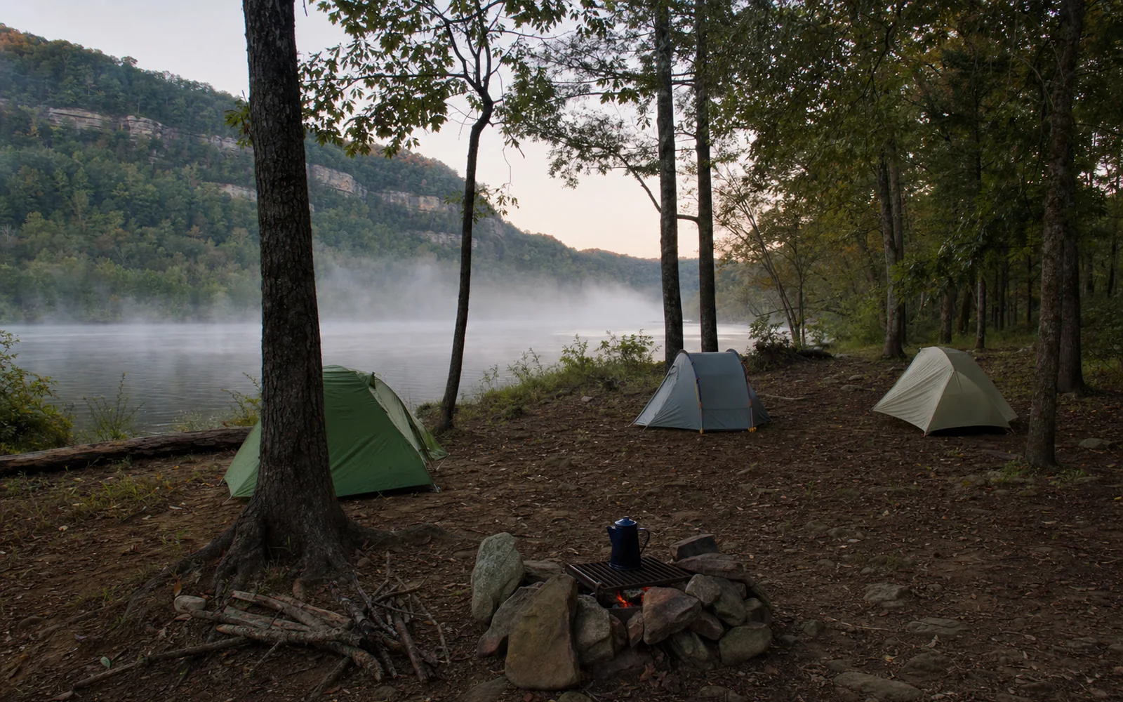 A small primitive campground on a river flat, three tents spaced among trees, morning fog on the river, a stone fire ring with a coffee pot, AI-generated illustration