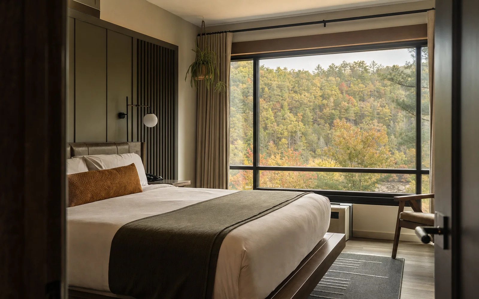 A modern hotel room with a king bed and a large window looking out on wooded hills, AI-generated illustration