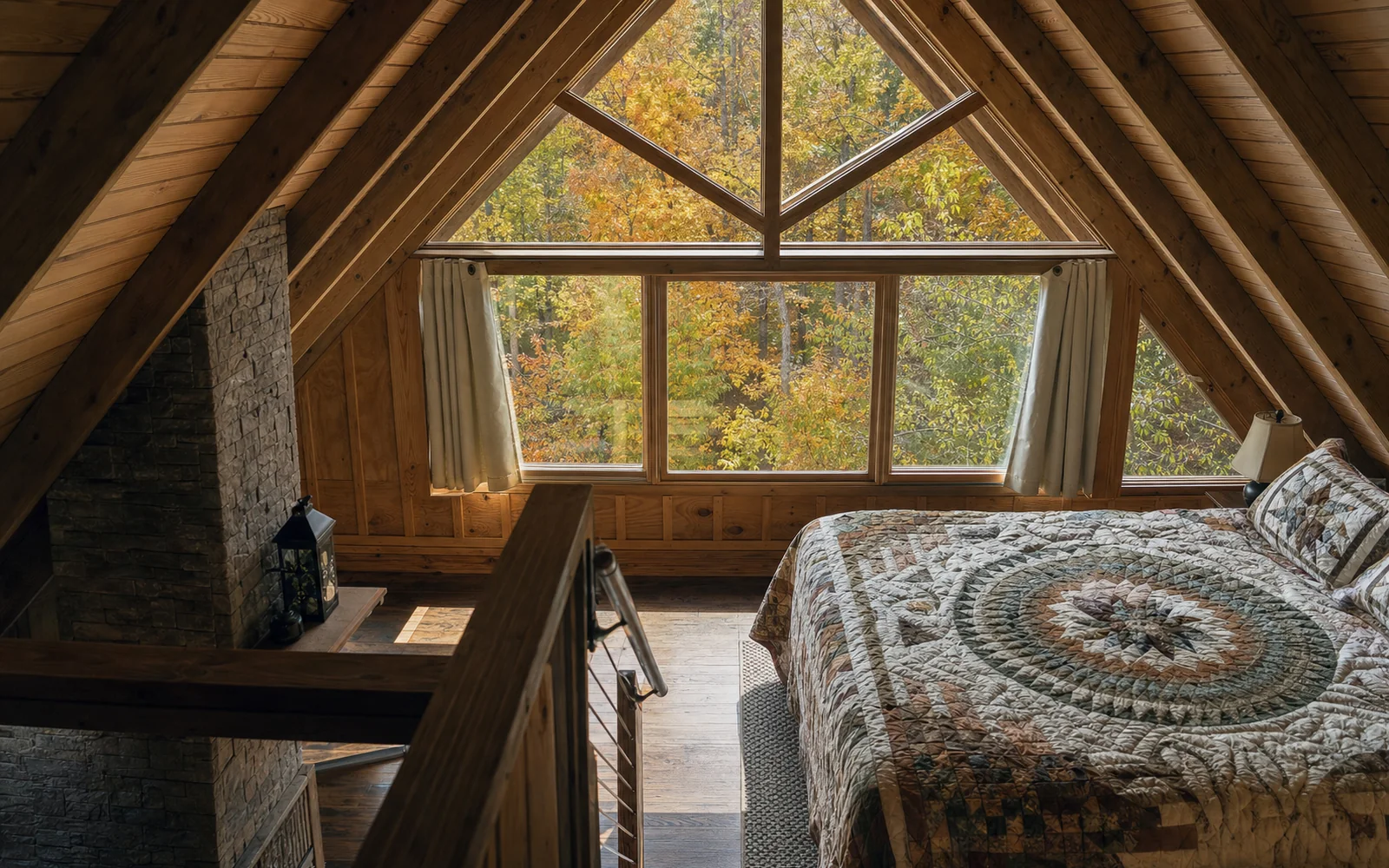 A cabin loft bedroom with a quilted bed and a big window looking into golden fall treetops, AI-generated illustration