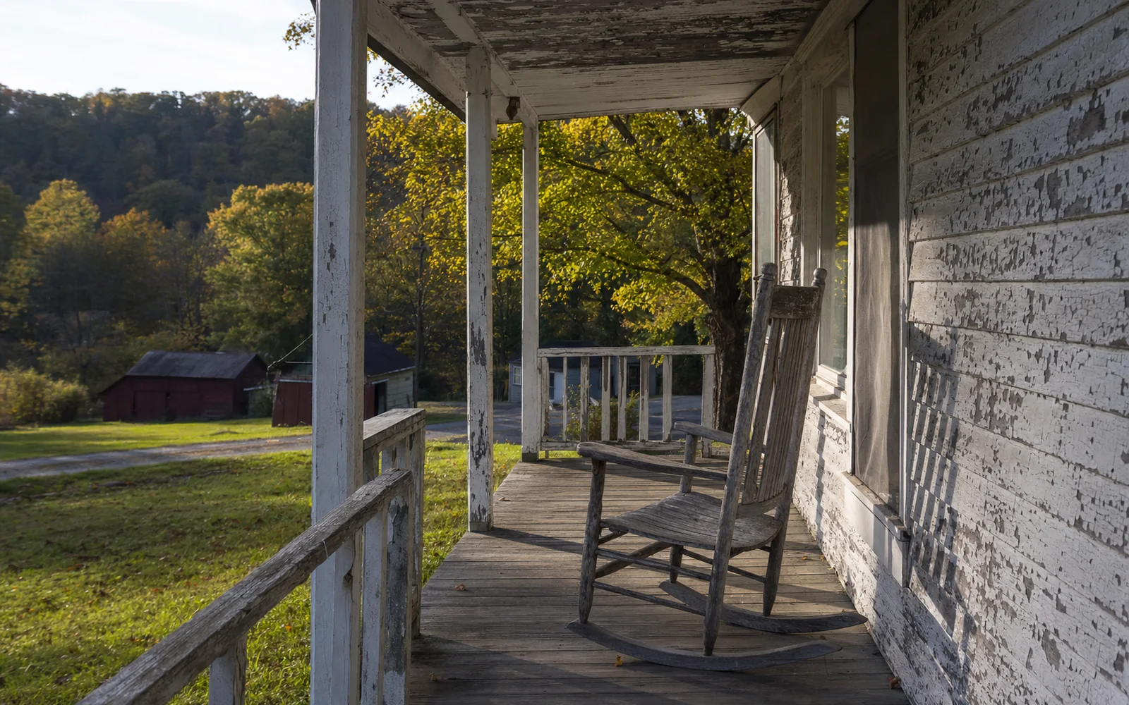 The weathered wooden porch of an old coal-camp house with a rocking chair, peeling paint, a hillside of hardwoods behind, AI-generated illustration